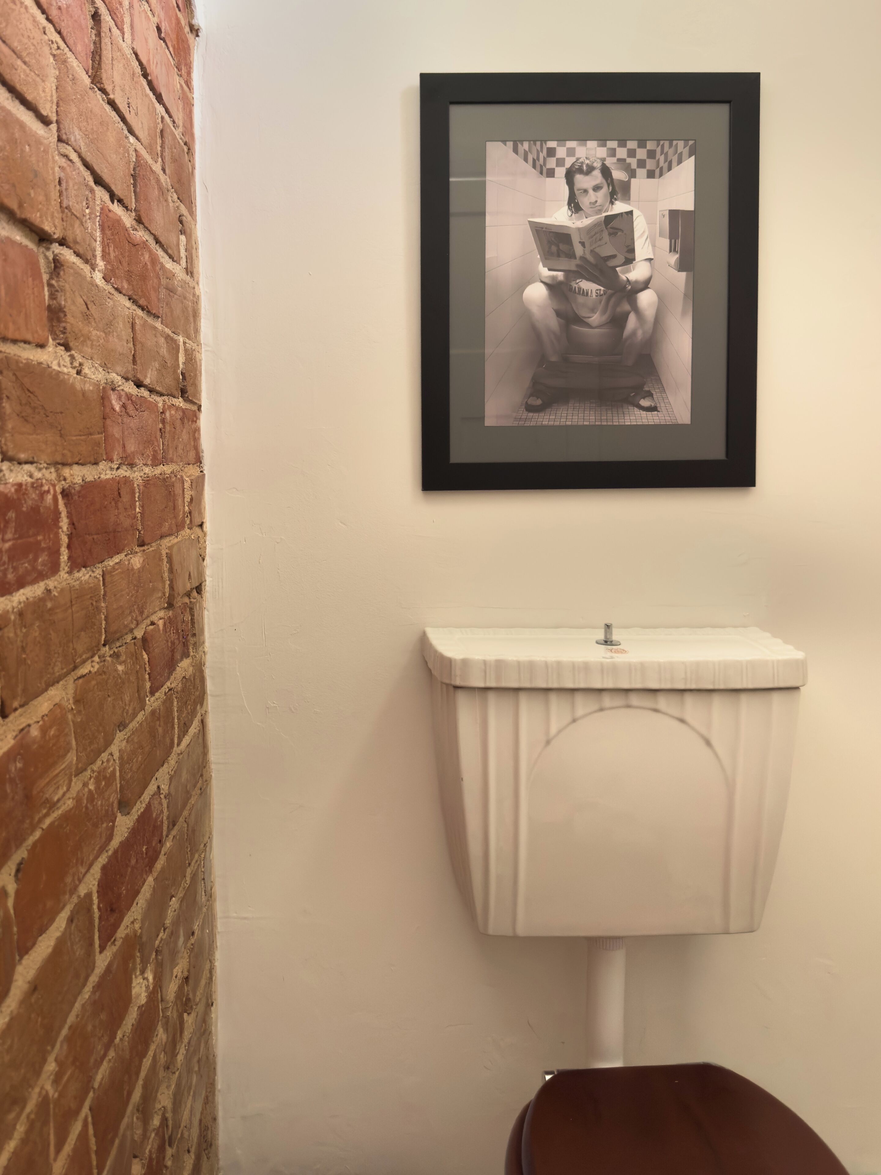 Casa de banho com sanita branca, fotografia a preto e branco emoldurada na parede, e parede de tijolos.