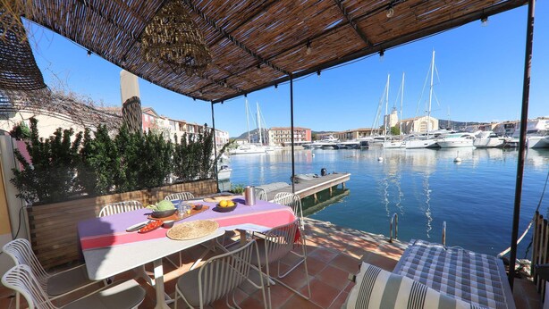 Un espace extérieur abrité, aménagé pour les repas, avec une table pour deux personnes, donnant sur une marina où sont amarrés des bateaux.