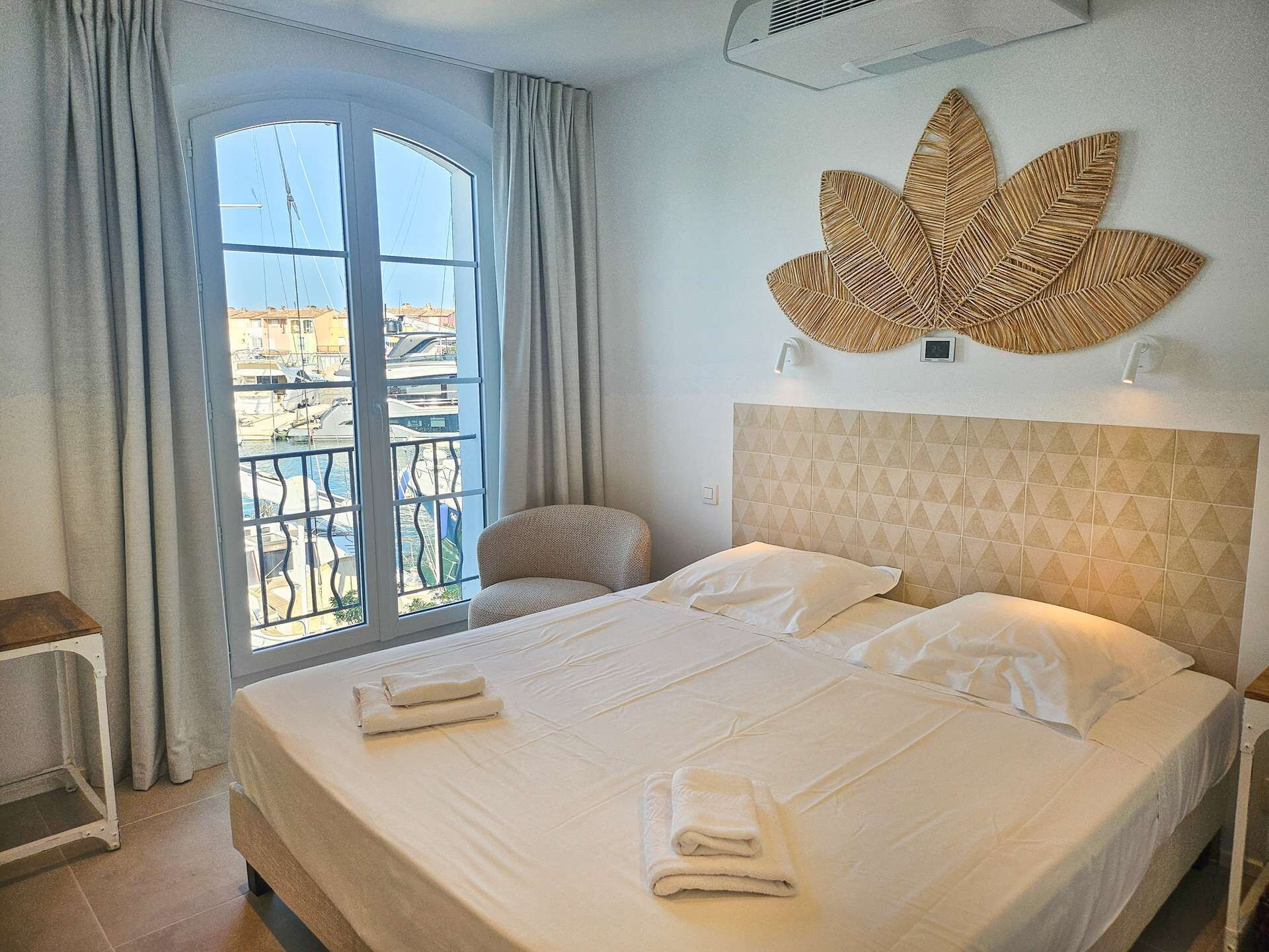 Una habitación de hotel con una cama, una silla, un ventanal con cortinas y un adorno en la pared.