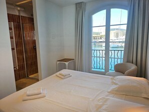 A hotel room with a bed, a small table, a chair, a window with a view of a marina, and a walk-in closet. - Elegant renovated house for 8 people, air-conditioned, with 14 m mooring and Wi-Fi (PORT GRIMAUD)