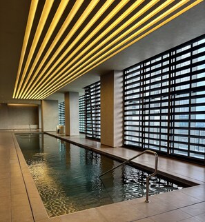 A modern indoor swimming pool with a long, narrow design, surrounded by large windows and a ceiling with linear lighting. - Century Spire Condominium  (Makati)