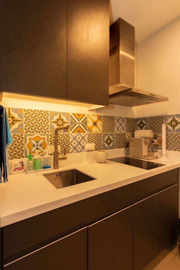 A modern kitchen with a stainless steel sink, a range hood, and a tiled backsplash with geometric patterns. - Century Spire Condominium  (Makati)