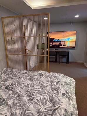 Une chambre à coucher avec un lit, un téléviseur diffusant une scène de coucher de soleil, un bureau avec des chaises et une cloison en bois.