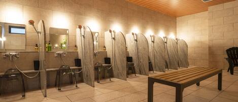 A modern bathroom with multiple shower stalls, a bench, and a tiled floor.
