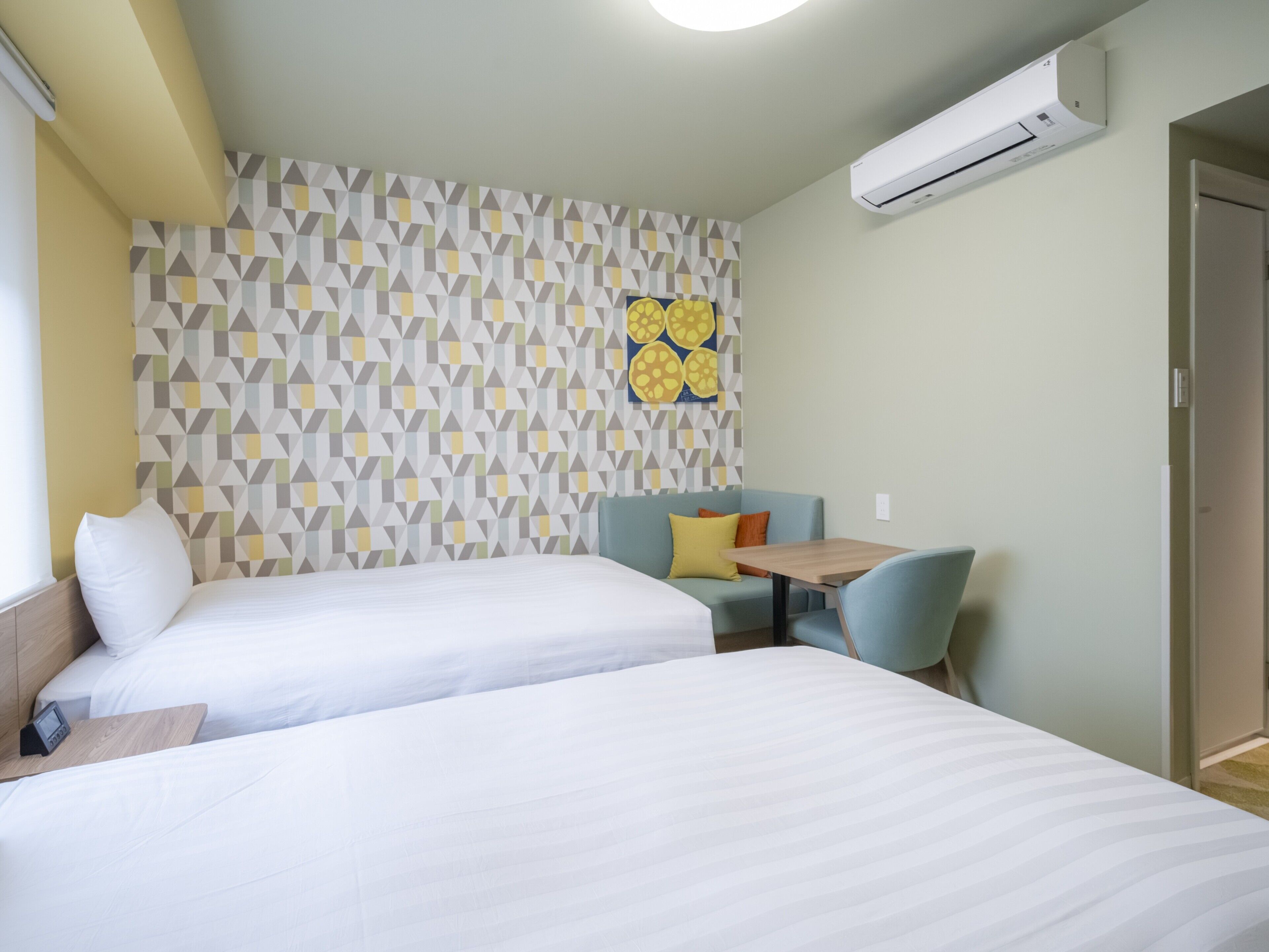 A hotel room with two beds, a small table, a sofa, and a wall with a geometric pattern.
