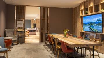 A modern dining area with a long wooden table, multiple chairs, and a television mounted on the wall.