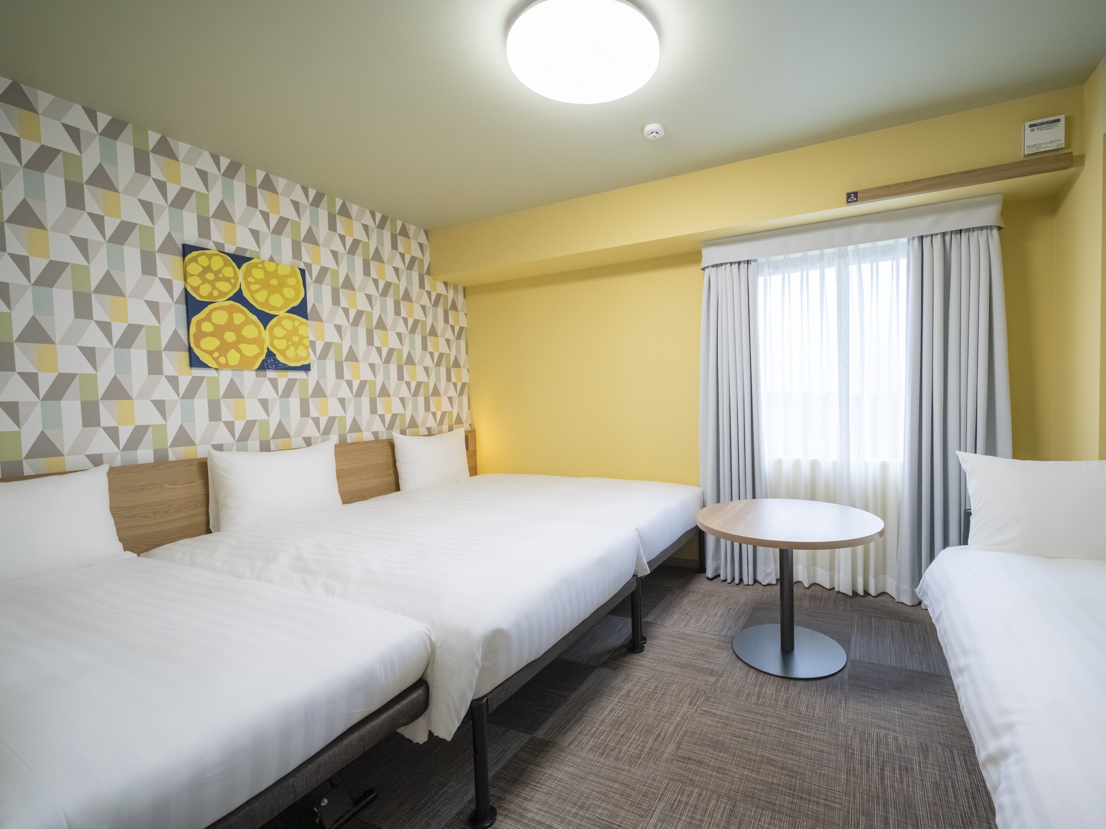 Et hotelværelse med to senge, et lille rundt bord, en væg med geometrisk mønster og en loftslampe.