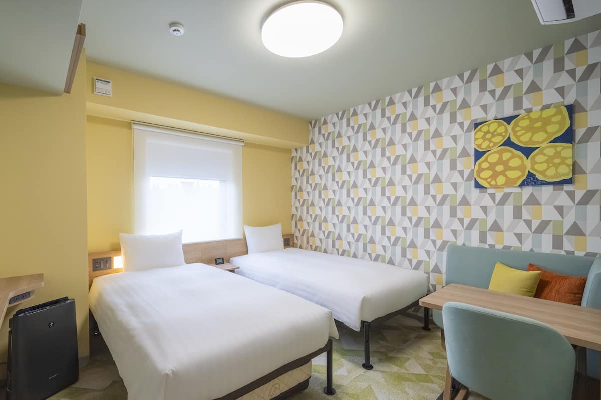 Habitación de hotel con dos camas, un escritorio, una silla y un papel tapiz estampado.