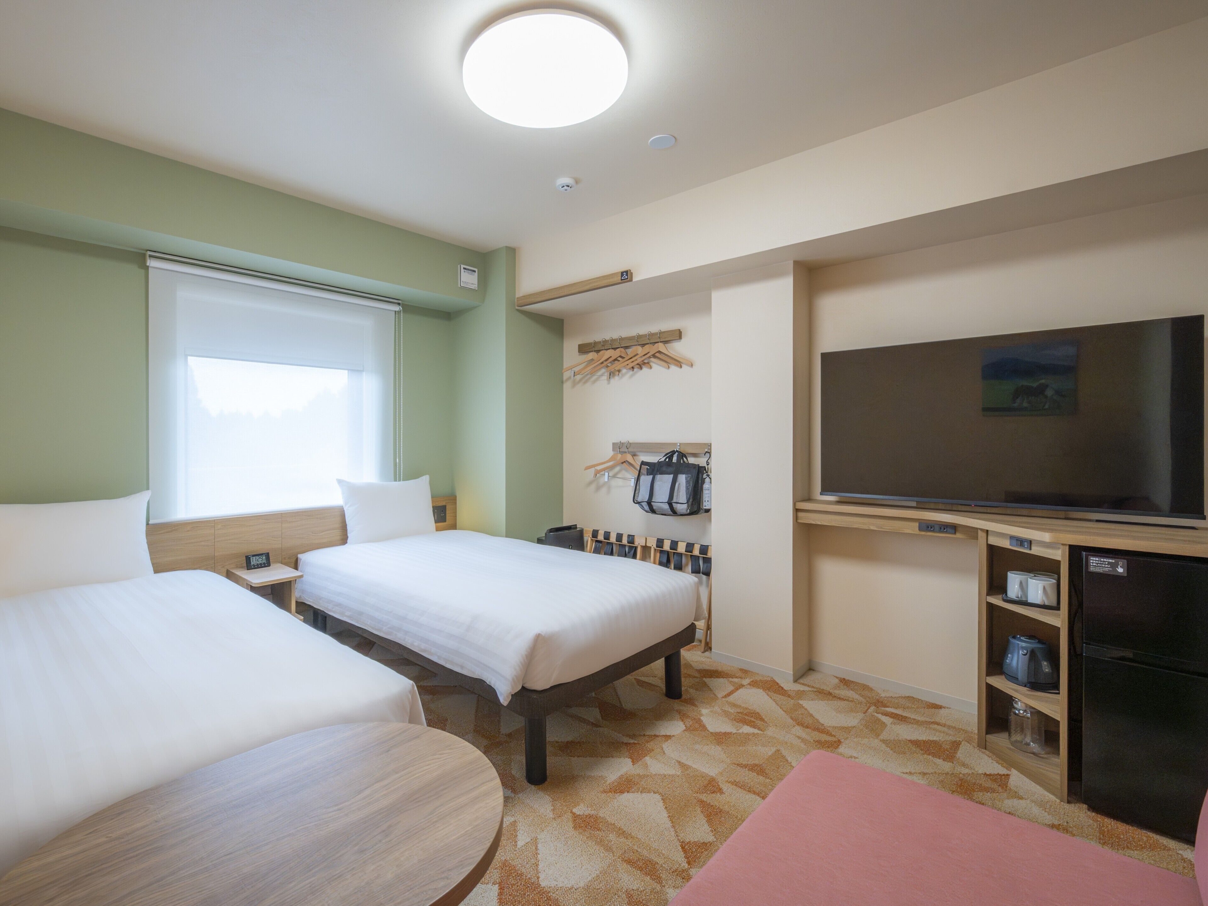 A hotel room with two beds, a TV, a desk with a computer, and a small refrigerator.