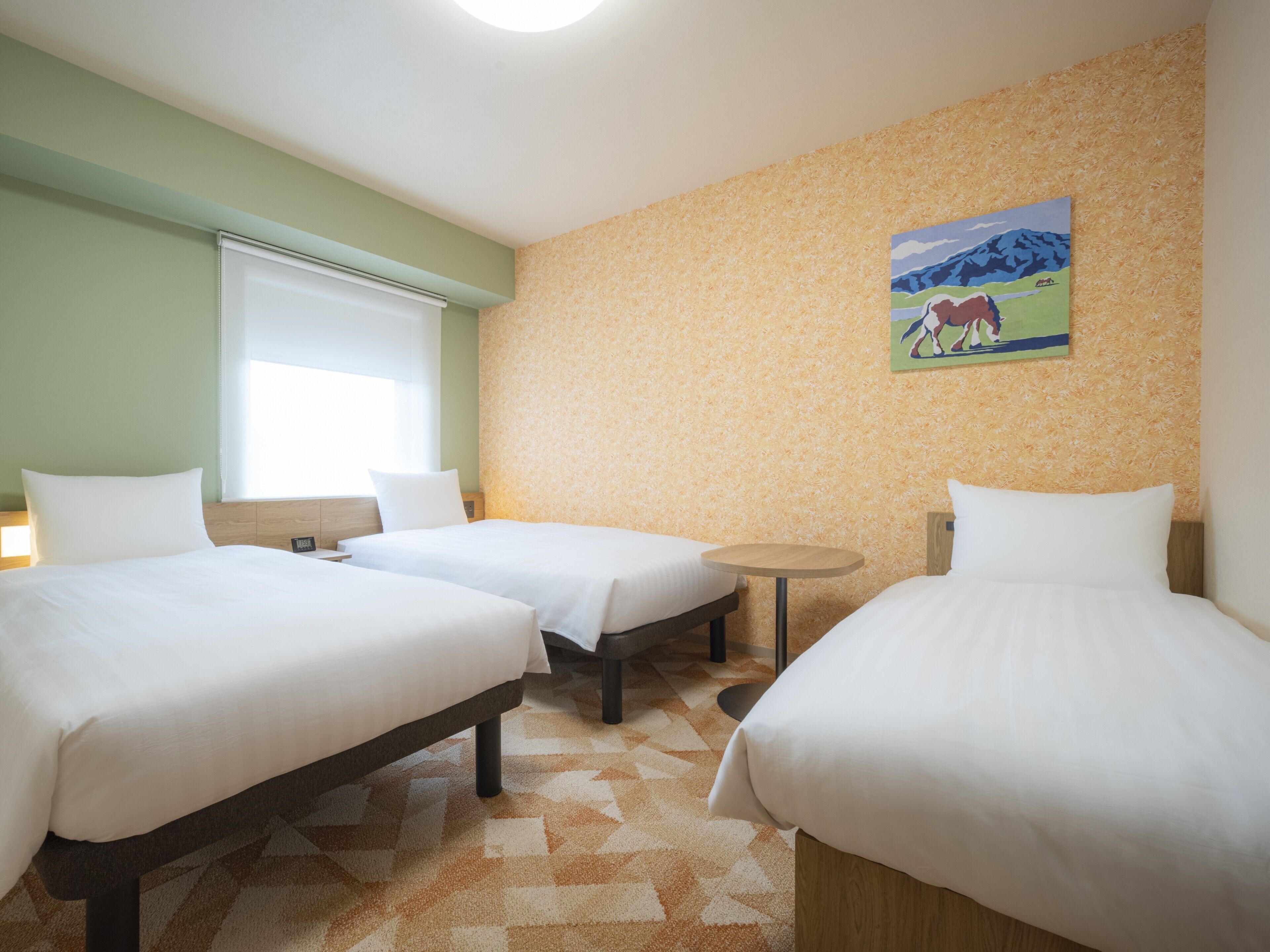 A hotel room with two beds, a small table, and a painting on the wall.