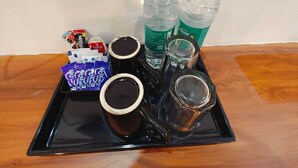 A tray with two bottles of water, two cups of coffee, a pack of coffee pods, and a glass of water. - Hotel Tapomay Retreat (Rishikesh)