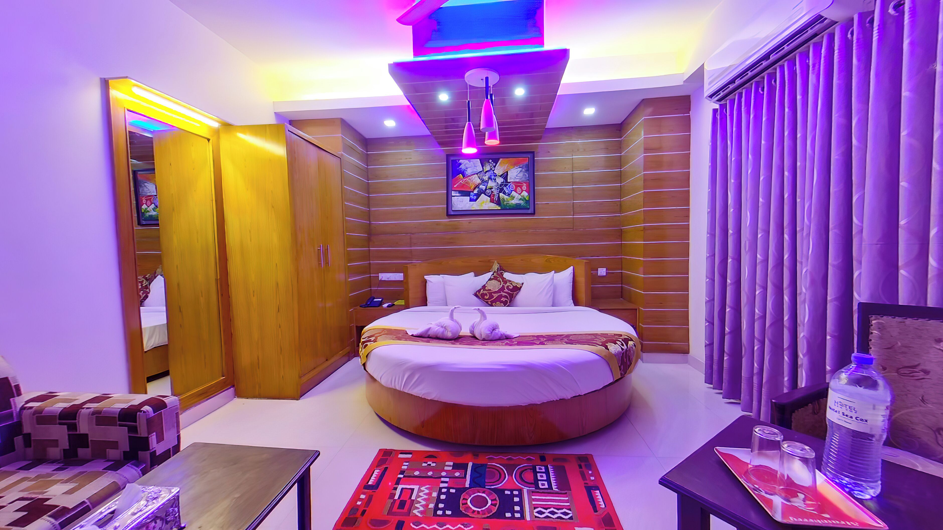 Una habitación de hotel con una cama, un armario de madera, una mesita y una botella de agua.