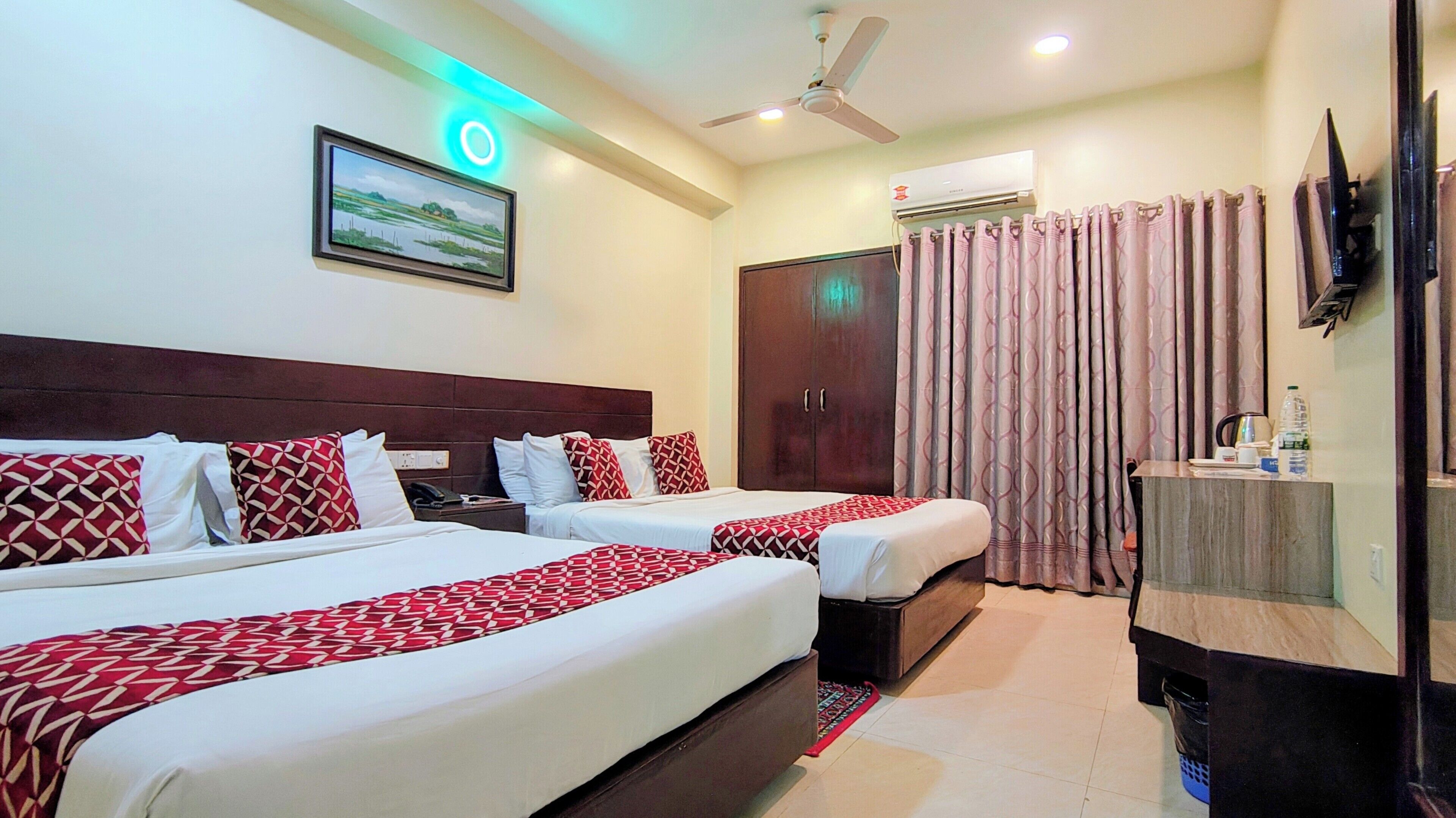 A hotel room with two beds, a ceiling fan, an air conditioning unit, a television, and a painting on the wall.