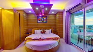 A hotel room with a large bed, wooden panel walls, a painting above the bed, and a view through a large window. - Hotel Sea Cox (Cox's Bazar)