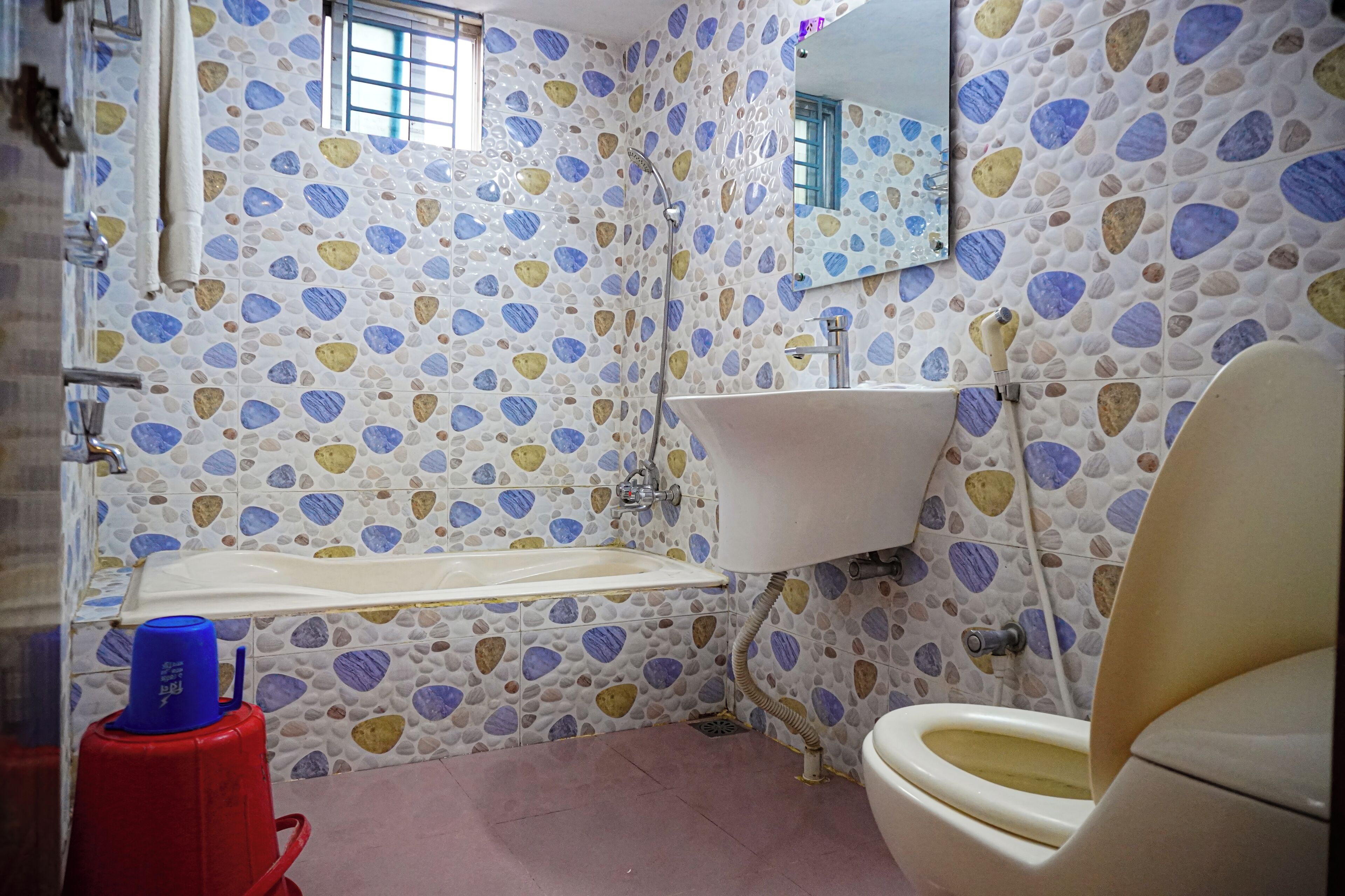 Un baño con lavamanos blanco, inodoro y ducha. Las paredes están revestidas con un diseño de piedrecita.