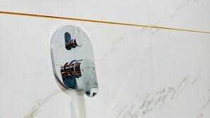 A bathroom with a white marble wall, a chrome faucet, and a mirror. - SAIRAM RESIDENCY (Khuldabad)