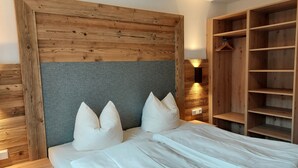 A bedroom with a wooden headboard, a grey accent wall, and a built-in wooden wardrobe with shelves. - Grundlsee vacation apartment - Charming vacation apartment right on the lakeshore (Mosern)