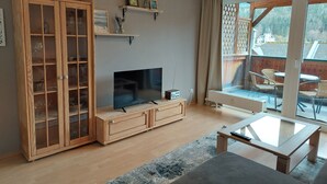 A living room with a TV, wooden cabinet, and a glass coffee table. - Grundlsee vacation apartment - Charming vacation apartment right on the lakeshore (Mosern)