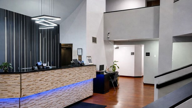A modern reception area with a wooden reception desk, a blue-lit counter, and a staircase leading to an upper level. - Layover Inn Boise Airport (Boise)
