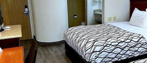 A hotel room with a bed, a desk, a chair, and a door.