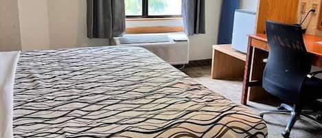 Une chambre d’hôtel comprenant un lit, un bureau, une chaise, une fenêtre avec des rideaux et une étagère fixée au mur, sur laquelle est posée une serviette.