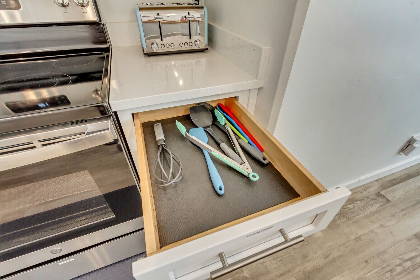 A kitchen with a toaster on the counter and a drawer with kitchen utensils.