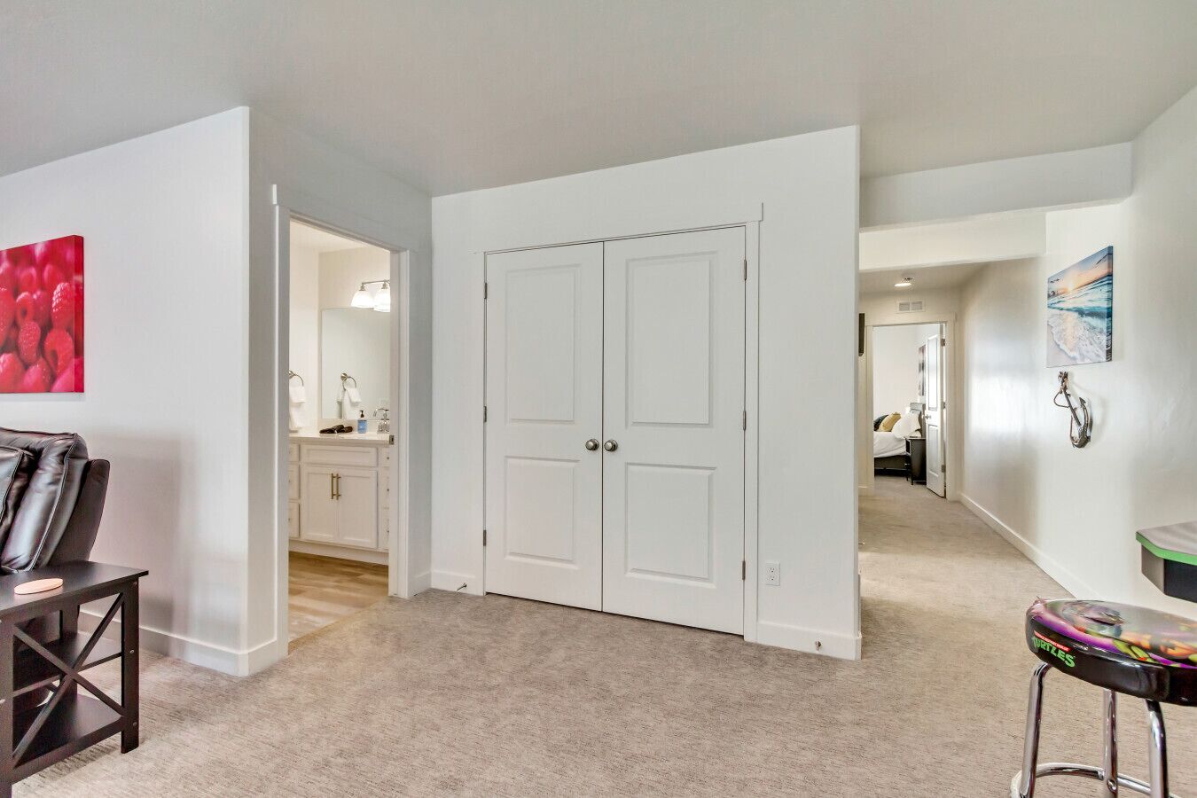 A hallway with a white door, a bathroom with a sink and mirror, and a bedroom with a bed and nightstand.