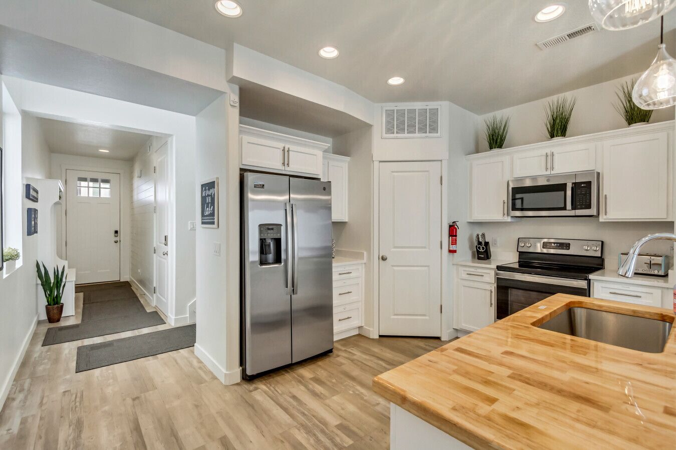 A modern kitchen with white cabinetry, stainless steel appliances, and a wooden countertop.