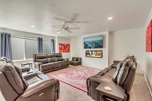 A modern living room with leather sofas, a ceiling fan, a fireplace, and artwork on the walls.