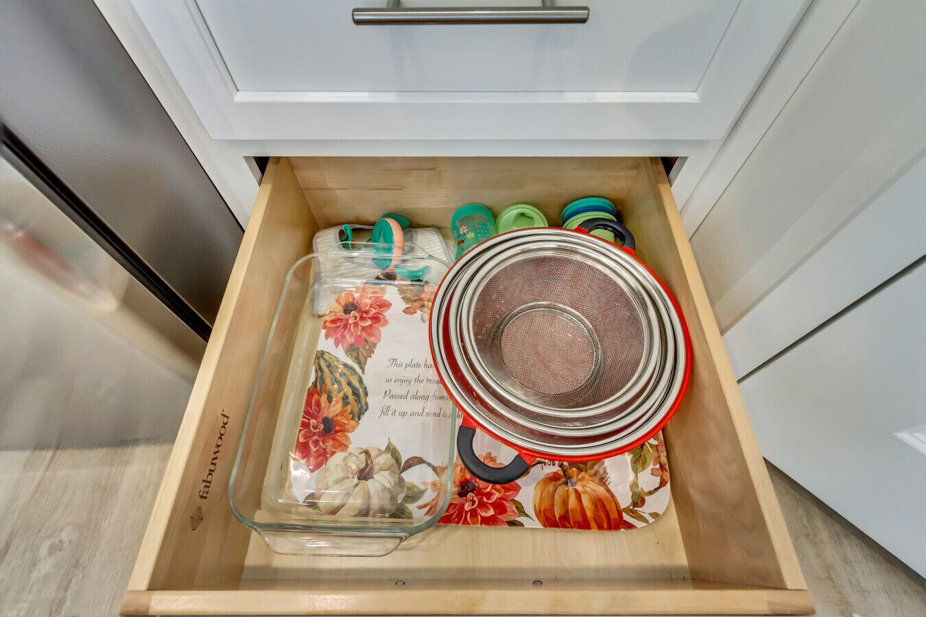 Un cajón de cocina con una fuente de vidrio, un colador rojo y varios tapones de colores.