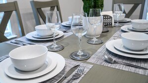 Une table à manger dressée avec de l’assiette blanche, des bols et des verres à vin, entourée de chaises.