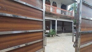 Une entrée fermée par un portail en bois et dotée d’un cadre en métal, qui mène à un patio couvert agrémenté de plantes en pot et offrant une vue sur un immeuble d’habitation.