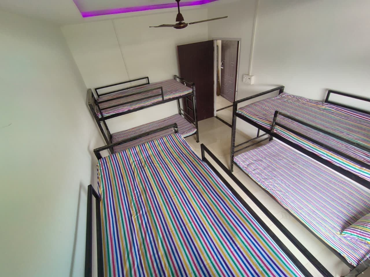 A dormitory room with bunk beds, a ceiling fan, and a door.