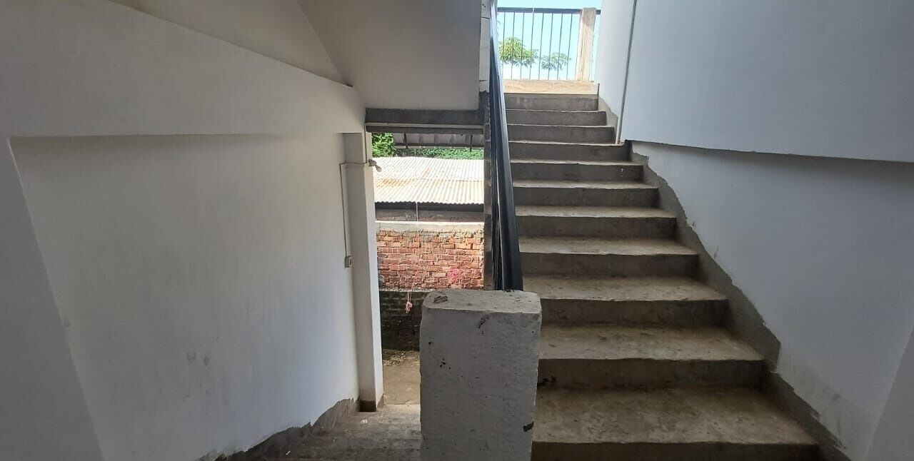 Una scala conduce a una zona esterna da cui si scorge un muro in mattoni e una recinzione metallica.
