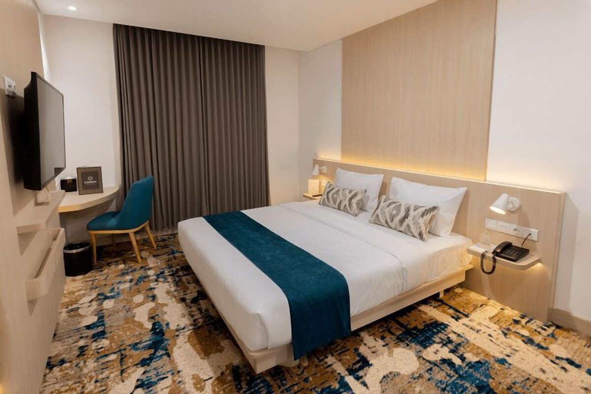 A hotel room with a bed, a desk, a chair, a TV, and a telephone.
