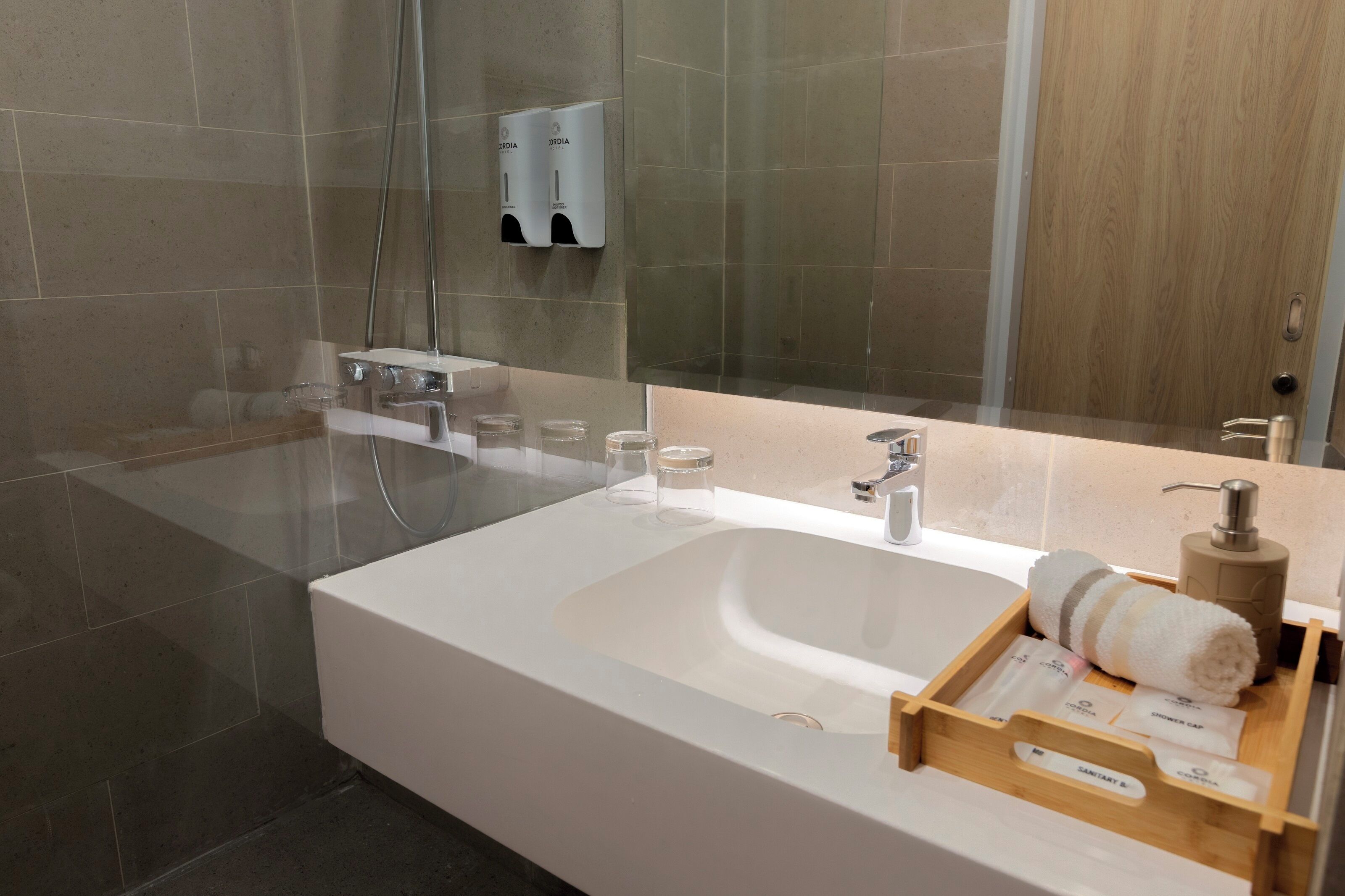 A modern bathroom with a large white sink, a glass shower enclosure, and a wooden door.