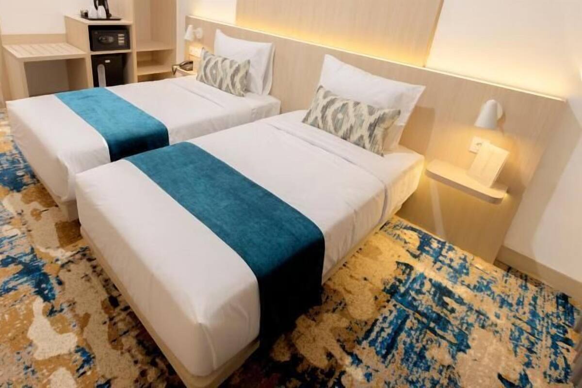 Ein Hotelzimmer mit zwei Betten, einem Schreibtisch, einem Sessel und einem Nachttisch.