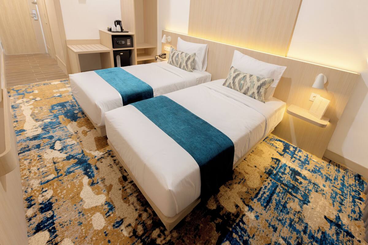 Ein Hotelzimmer mit zwei Betten, einem Schreibtisch und einem Nachttisch mit Lampe.