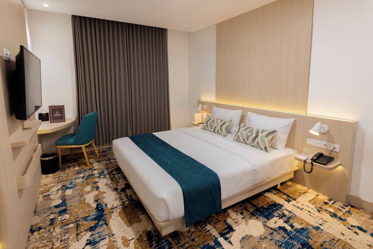 Ein Hotelzimmer mit Bett, Schreibtisch, Stuhl, Fernseher und Telefon auf dem Nachttisch.