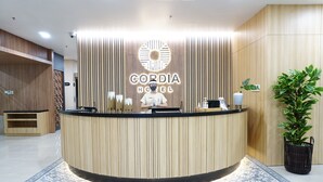 A hotel reception desk with a modern design, featuring vertical wooden panels and a logo above the counter. - Cordia Hotel Yogyakarta  (Temon)