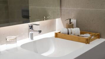 Un baño moderno con lavamanos blanco, grifo cromado y plato para jabón de madera.