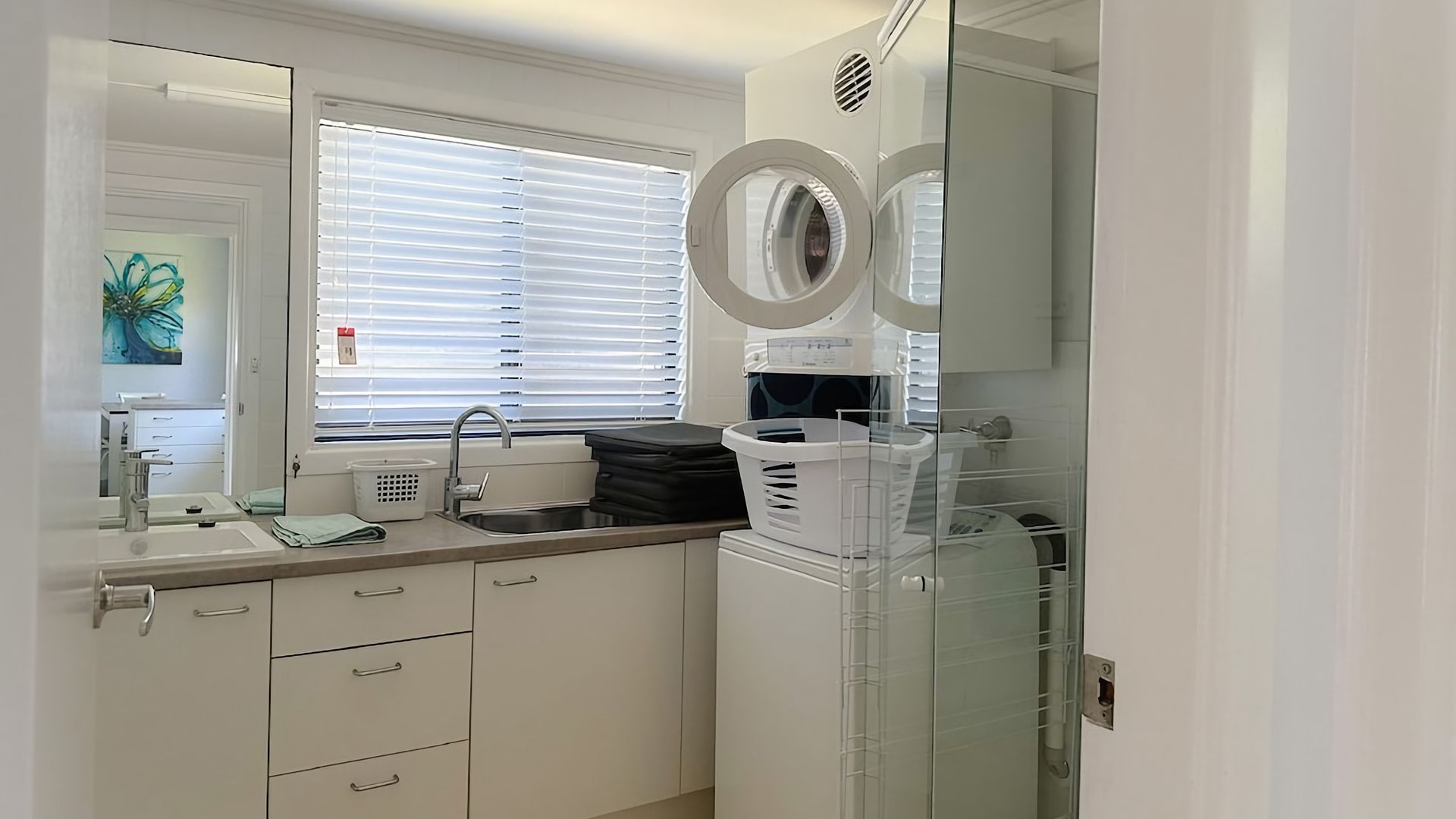 A modern bathroom with a large mirror, a sink, and a window with blinds.