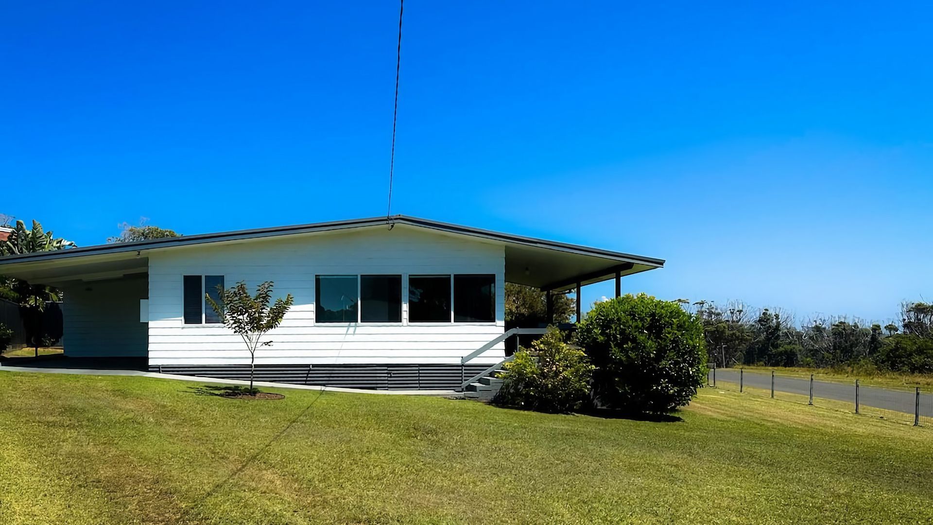A single-story house with a flat roof, a covered porch, and a small tree in the front yard.