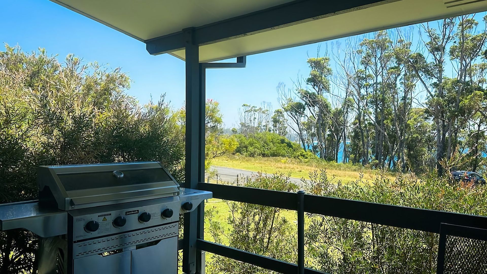 A barbecue grill on a balcony with a view of a road and trees.