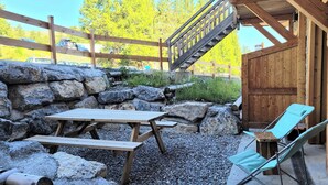 Un'area salotto esterna rustica con un tavolo e sedie di legno, circondata da rocce e tronchi.
