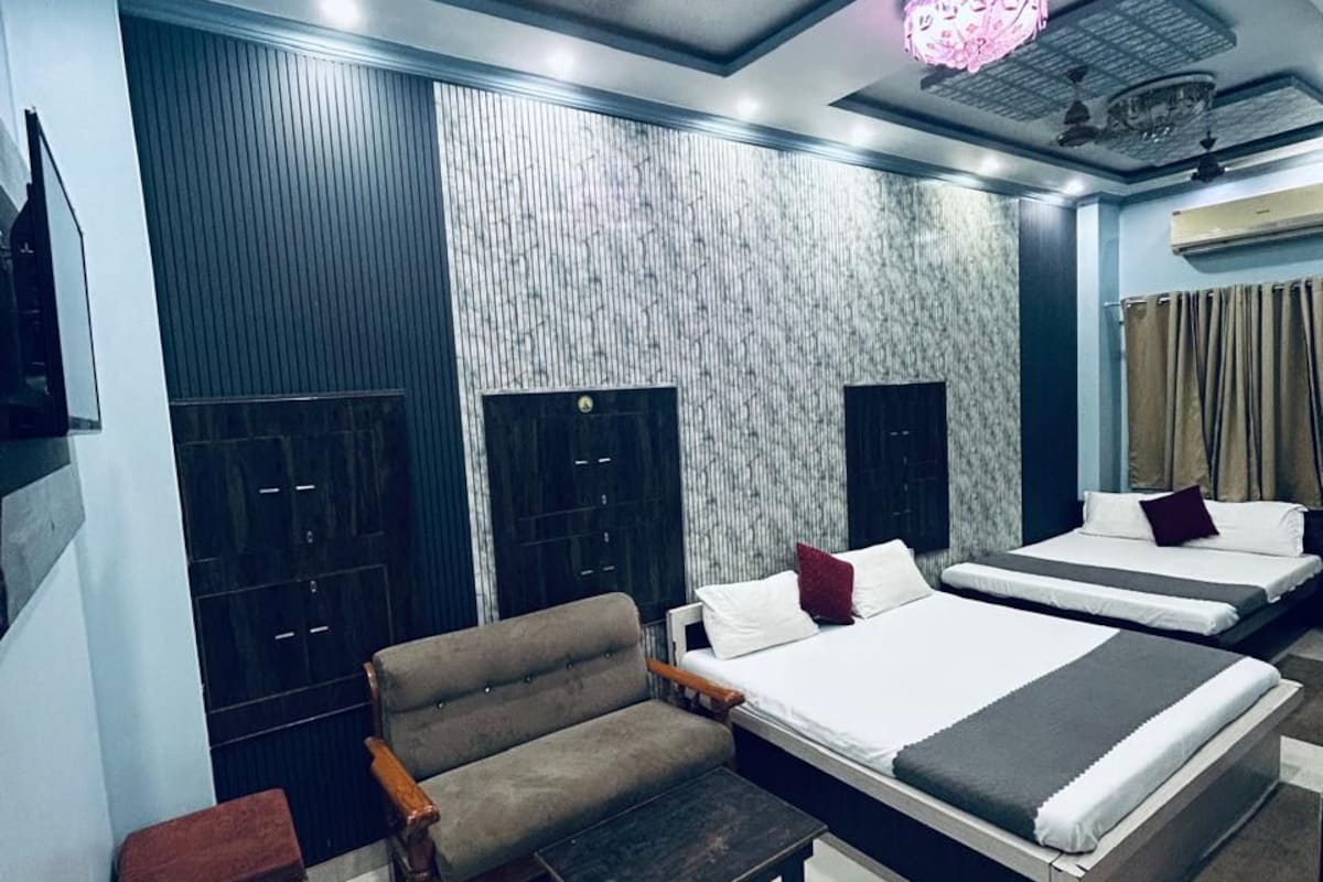 Une chambre d’hôtel moderne avec un canapé, deux lits, une petite table et un luminaire décoratif au plafond.