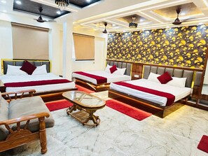 A hotel room with three beds, a glass coffee table, and a red carpet. - Hotel Aditya (Varanasi)