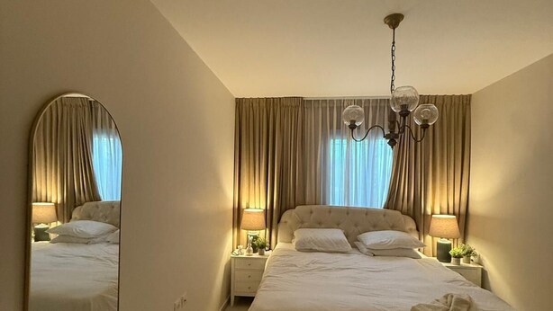 A hotel bedroom with a large bed, two bedside tables, a mirror, and a chandelier.