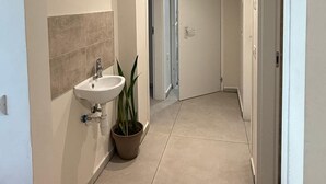 A narrow hallway with a white sink and a potted plant, leading to a door at the end.