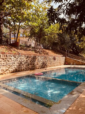 Una piscina con muro in pietra e solarium in legno.